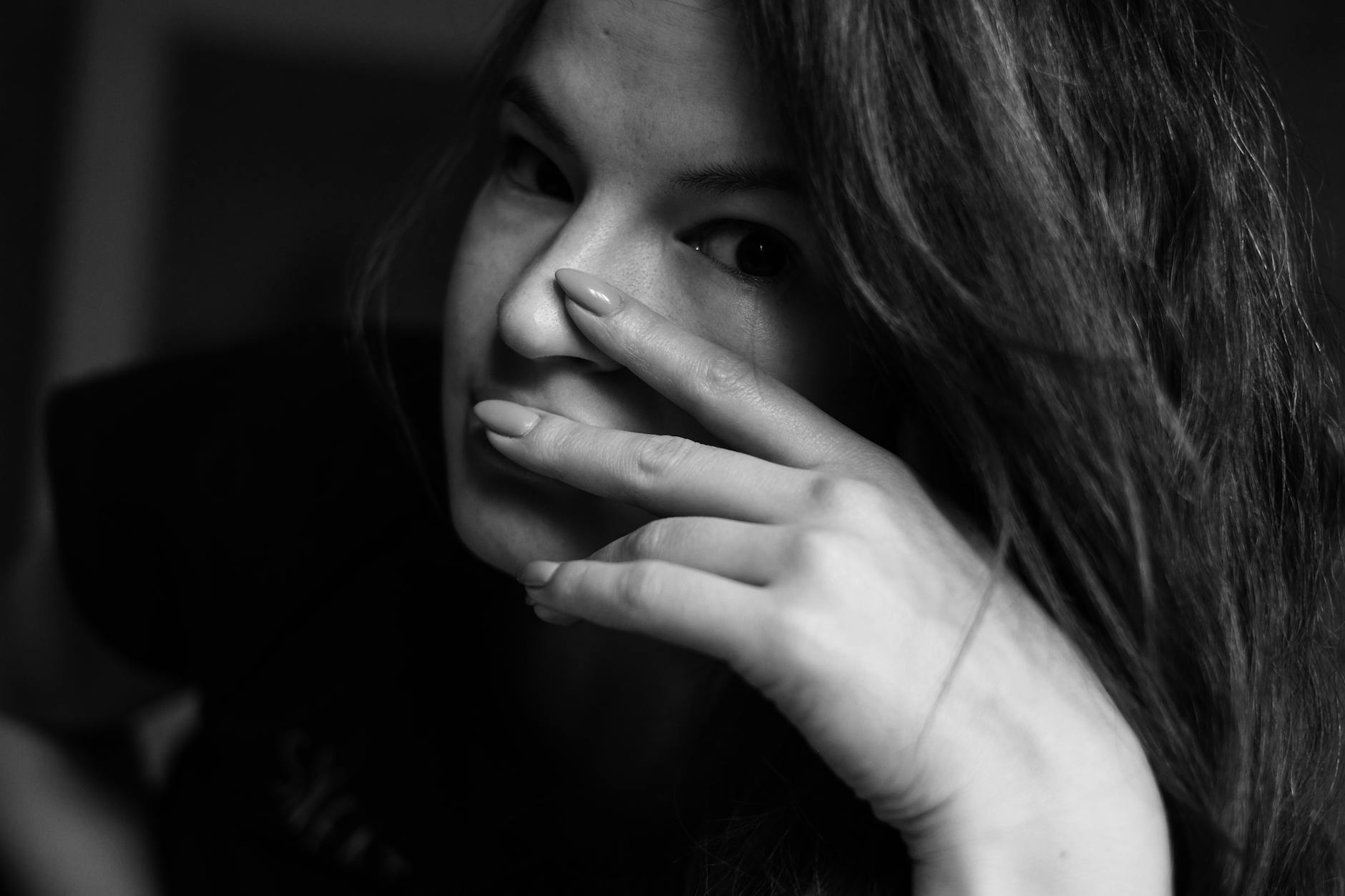grayscale photo of woman covering her face with her hand
